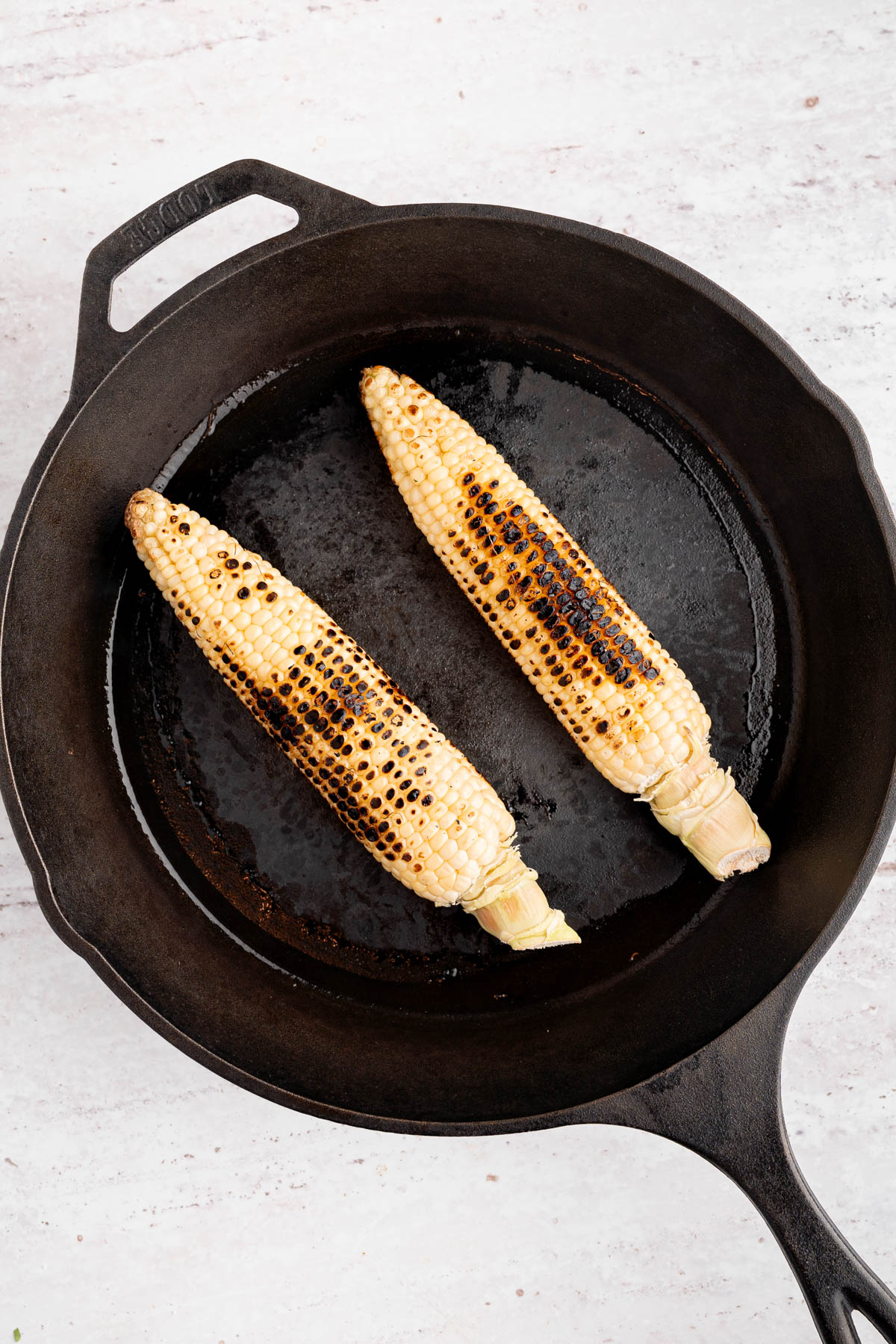Two charred pieces of corn in a cast iron skillet.