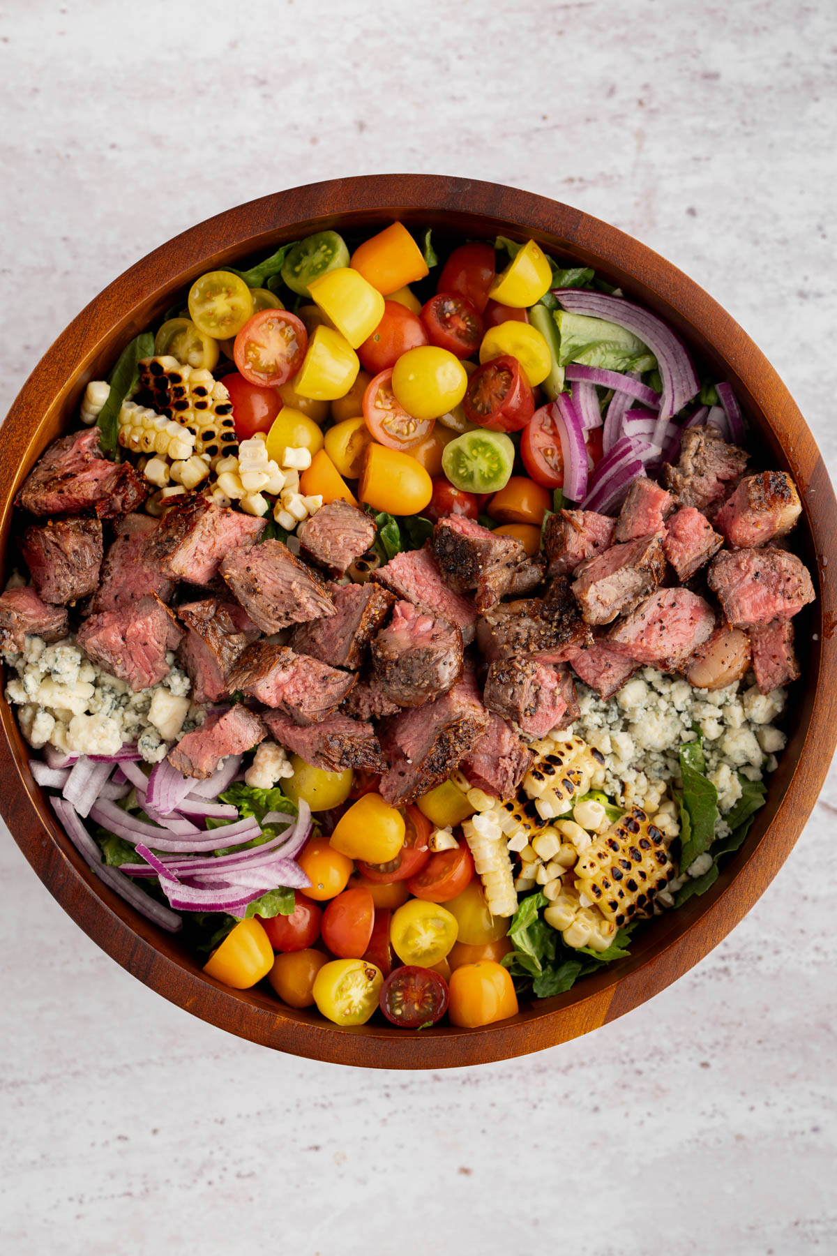 The fully assembled steak salad without the dressing in a bowl on a white countertop.
