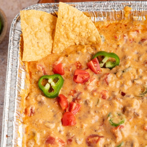 Two tortilla chips sit in a pan of grilled rotel dip that is garnished with a sliced jalapenos.