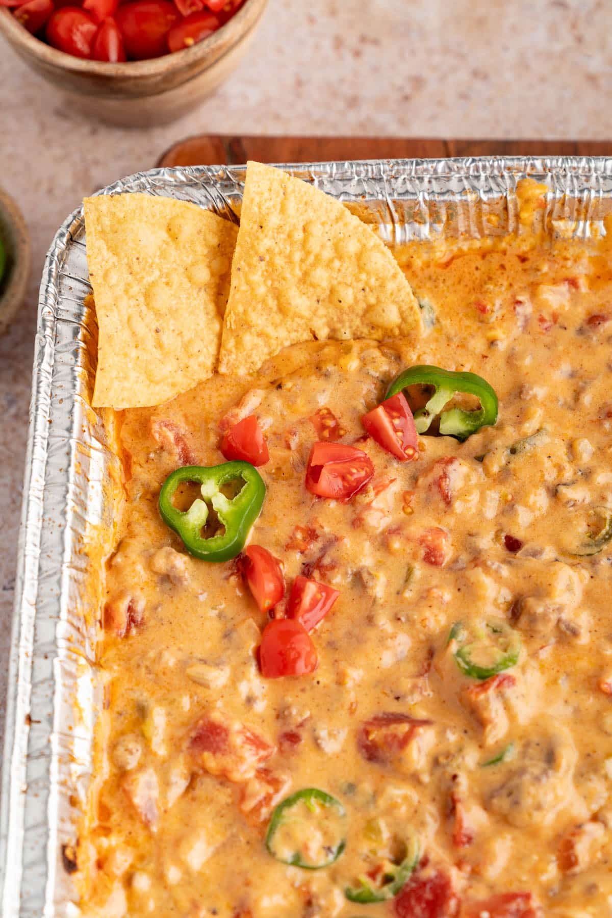 Two tortilla chips sit in a pan of grilled rotel dip that is garnished with a sliced jalapenos.