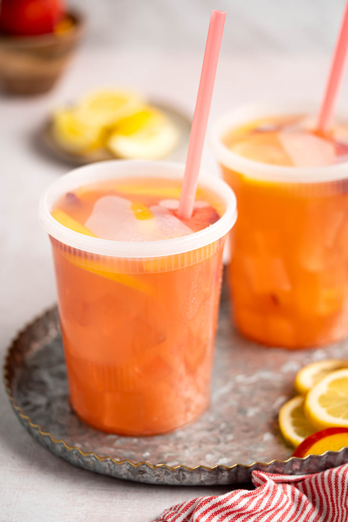 The peach lemonade in extra large containers with a straw in them.