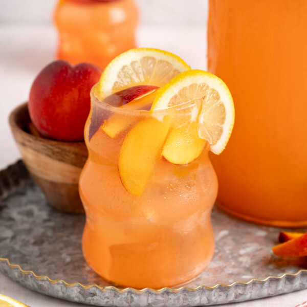 Two glasses of peach lemonade sit on a serving tray next to the pitcher.