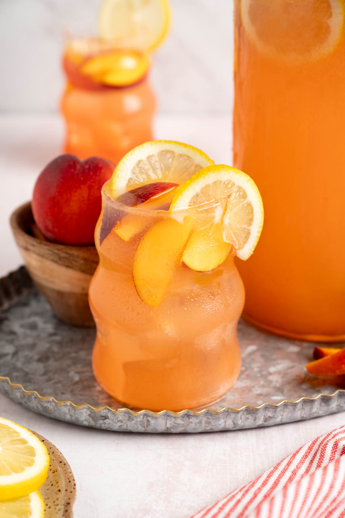 Two glasses of peach lemonade sit on a serving tray next to the pitcher.