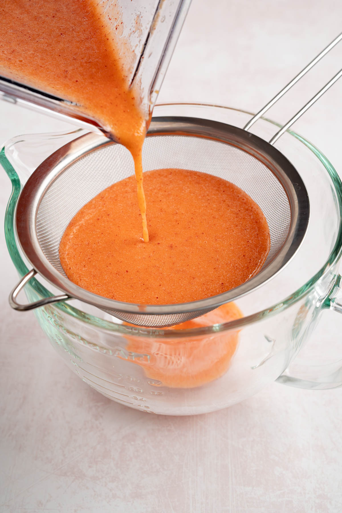 The peach syrup is poured through a strainer into a bowl.