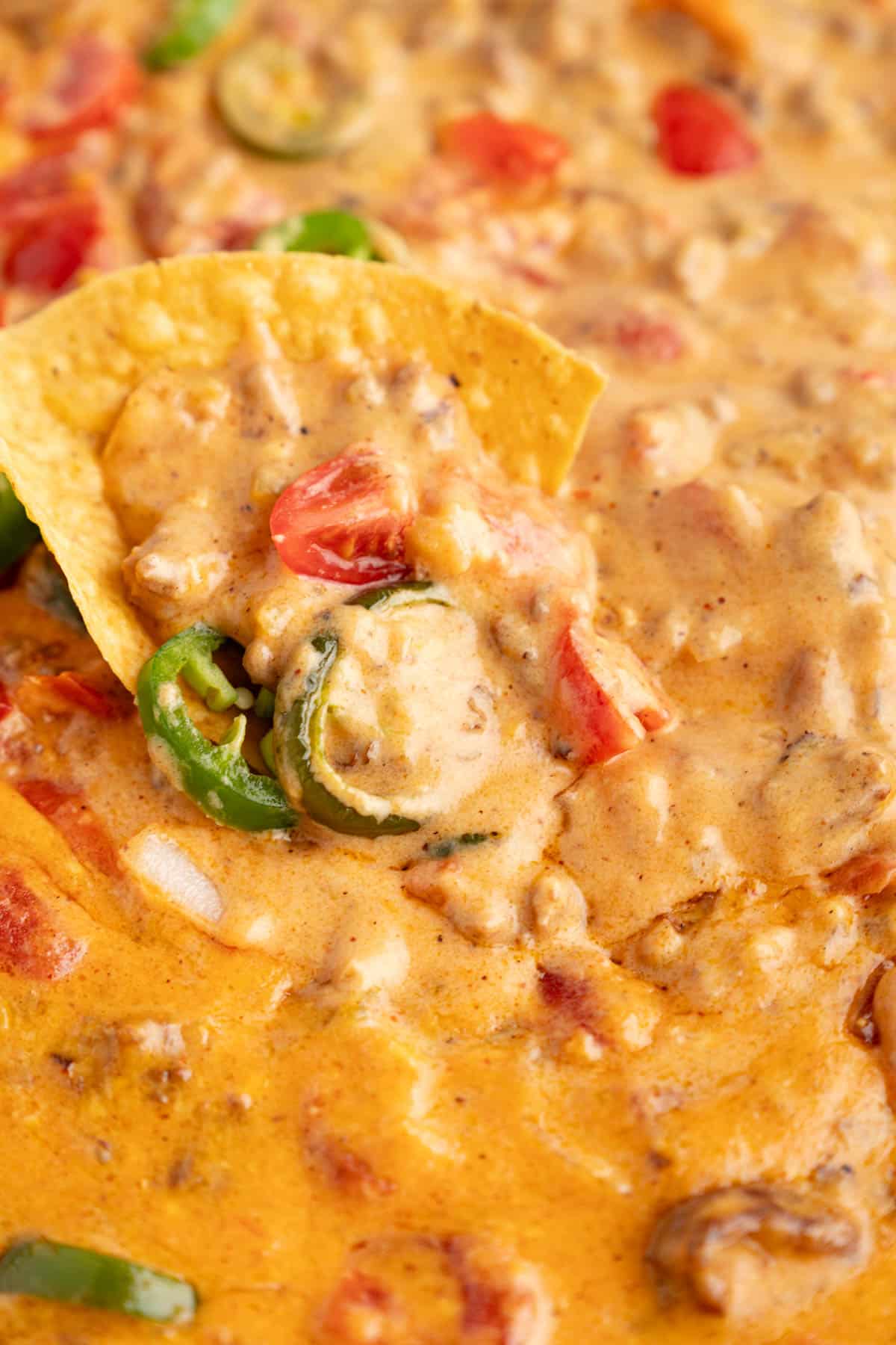 A tortilla chip sits in a pan of rotel dip dip.