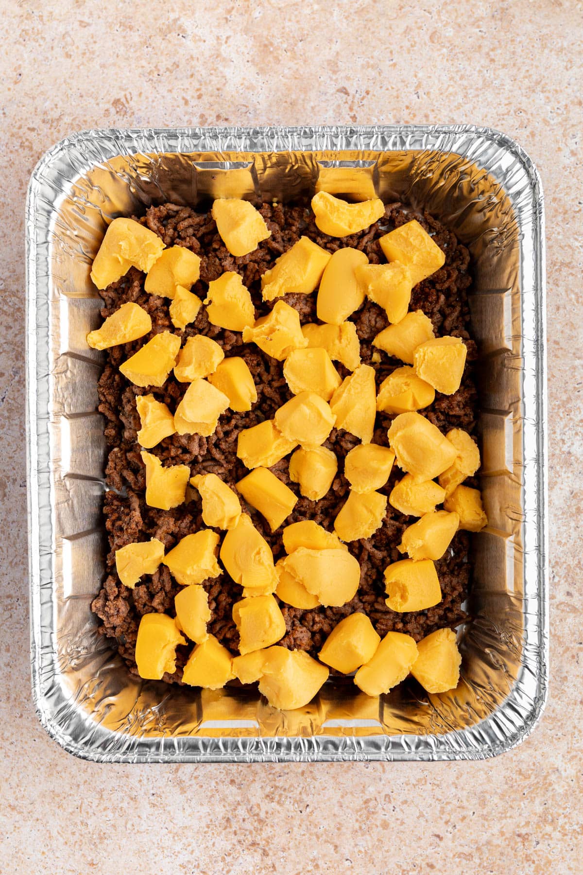 The velveeta cheese on top of the ground beef in the baking pan.