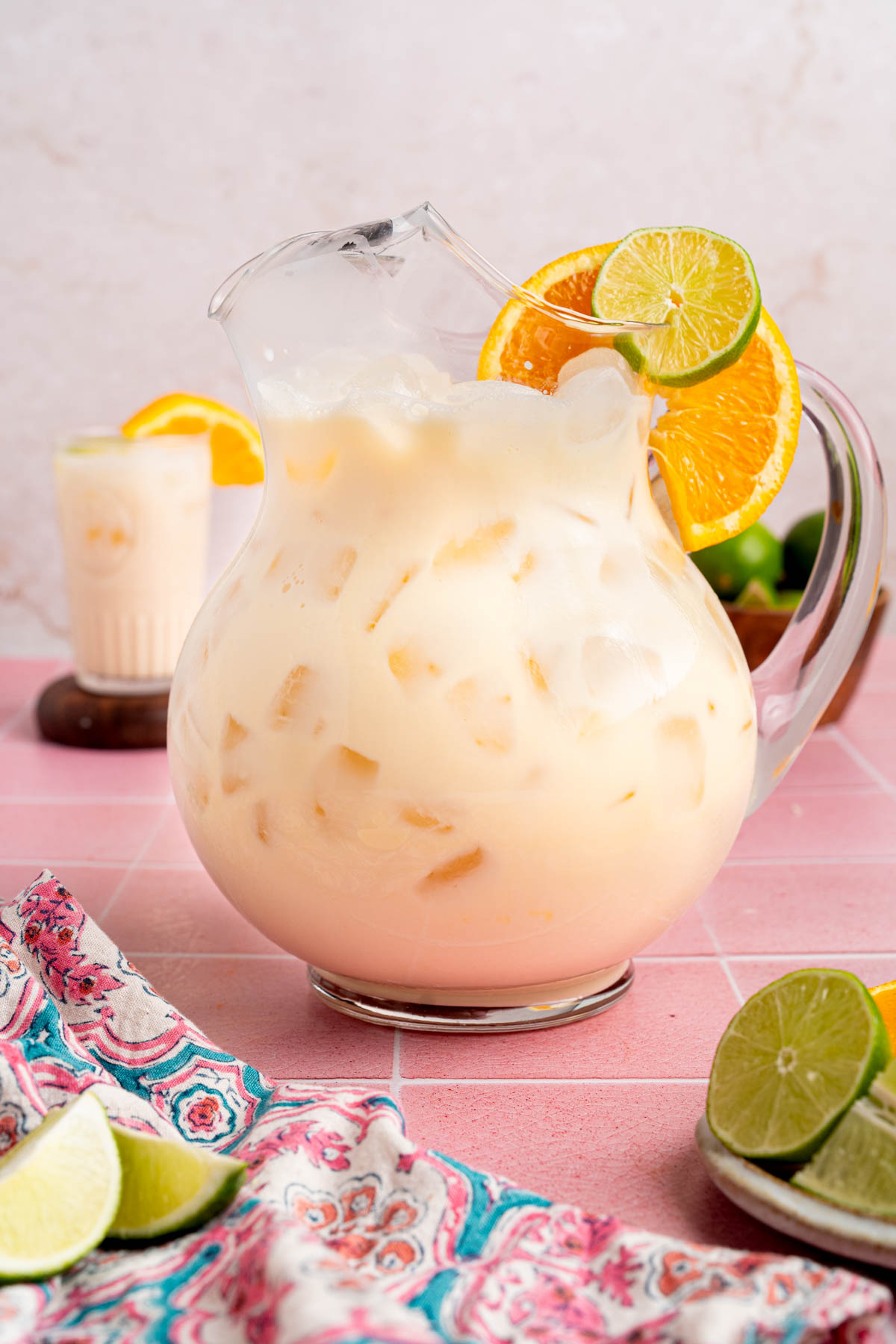A pitcher of morir sonando on a countertop garnished with a slice of orange and lime.