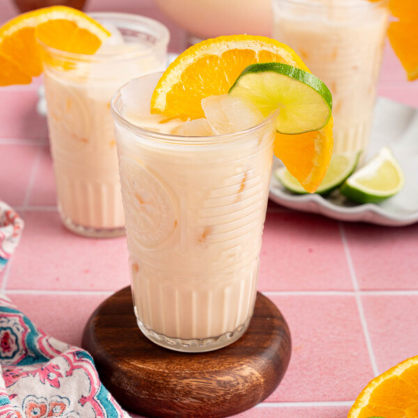 Three glasses of morir sonando on a countertop with a pitcher for serving.