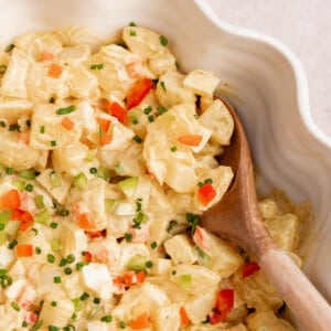 A spoon rests in a serving bowl with the puerto rican potato salad (ensalada de papa.)