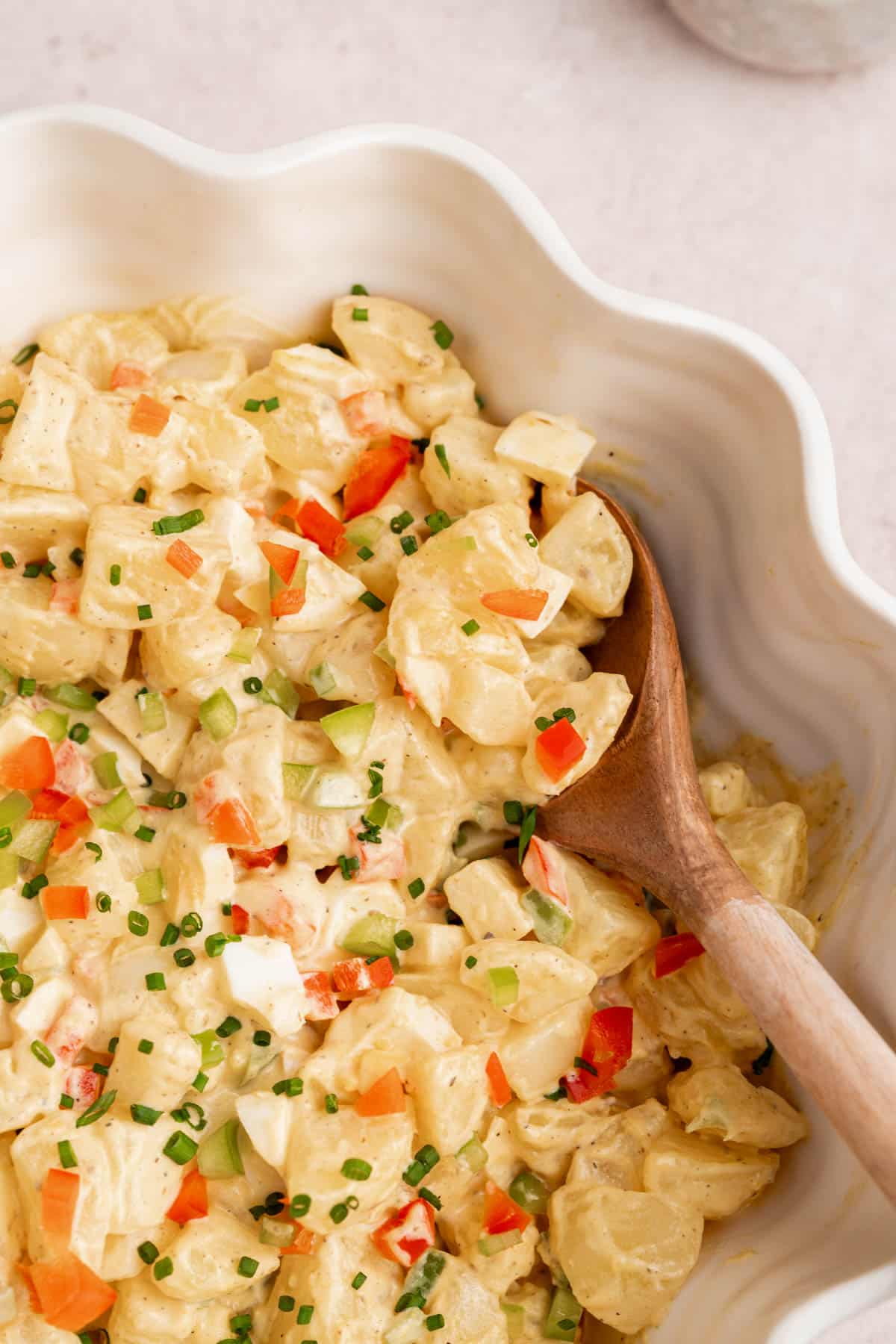 A spoon rests in a serving bowl with the puerto rican potato salad (ensalada de papa.)