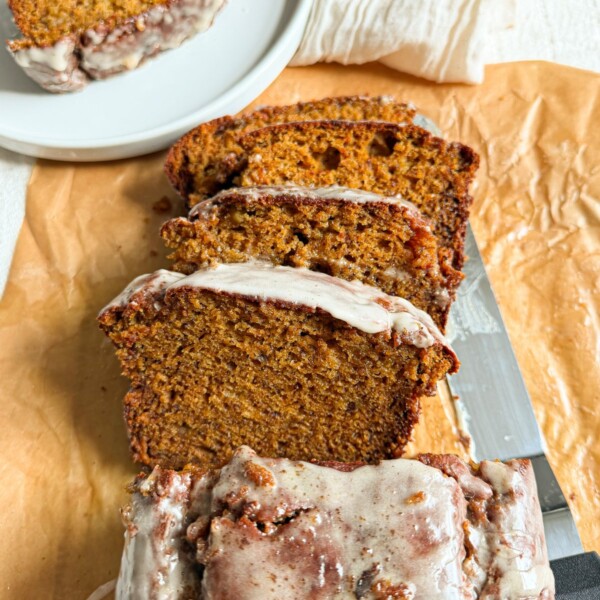 Brown butter sweet potato banana bread sliced on parchment paper with glaze dripping down the sides.