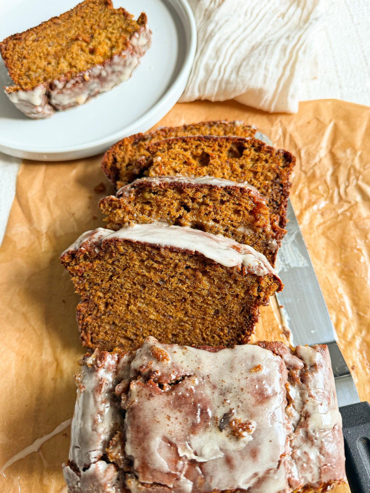 Brown butter sweet potato banana bread sliced on parchment paper with glaze dripping down the sides.