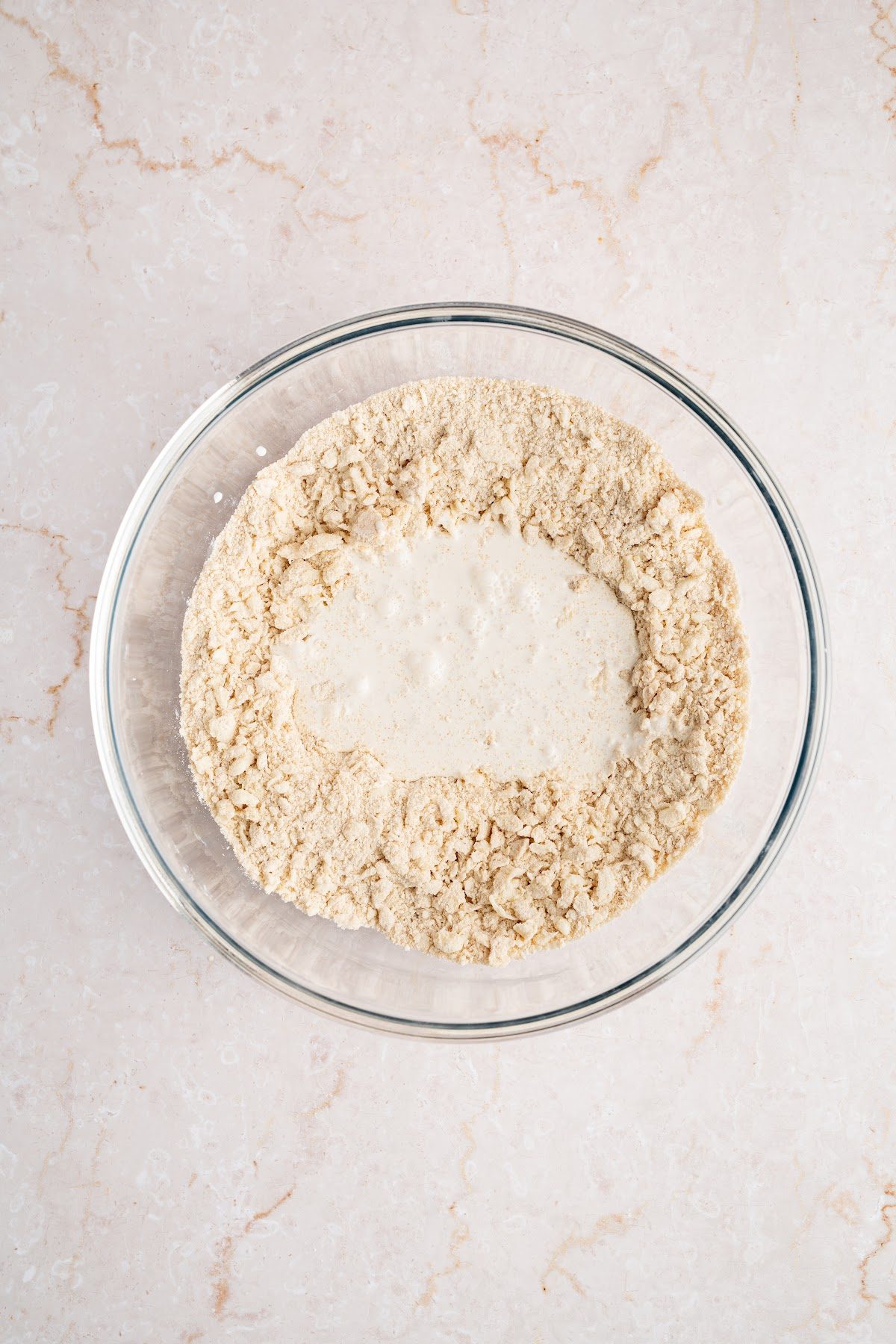 Heavy cream and vanilla being poured into the crumbly biscuit topping mixture