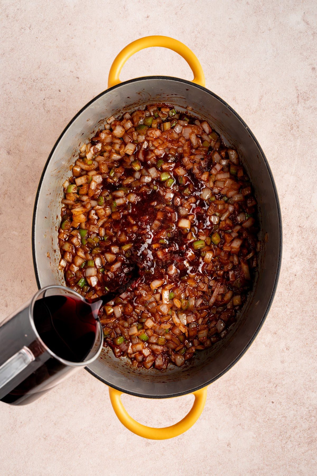 Red wine being poured into a Dutch oven of cooked onion and celery to deglaze the pan