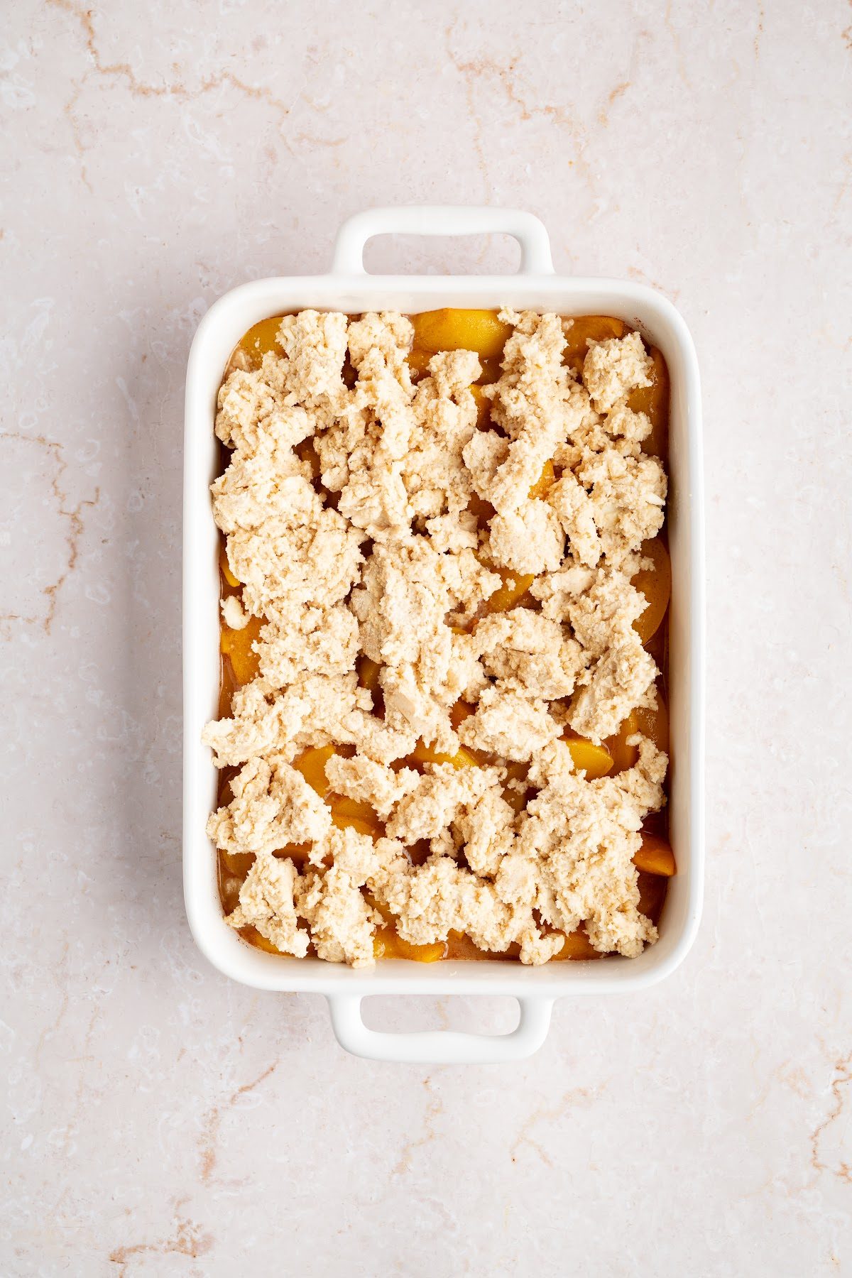 Spoonfuls of biscuit dough dropped evenly over the peach filling in a baking dish before baking
