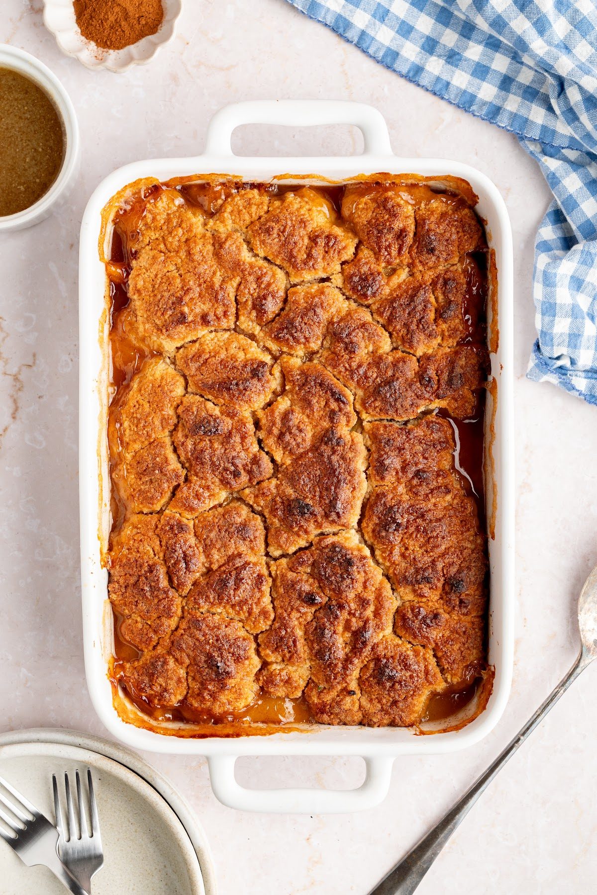 A whole biscuit top peach cobbler in a white baking dish with a deep golden brown biscuit top