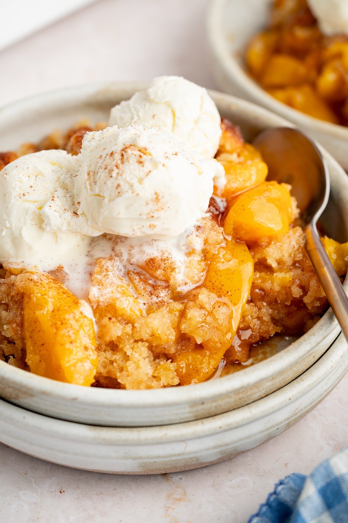 Biscuit top peach cobbler served warm in a bowl with two scoops of vanilla ice cream melting over the peaches