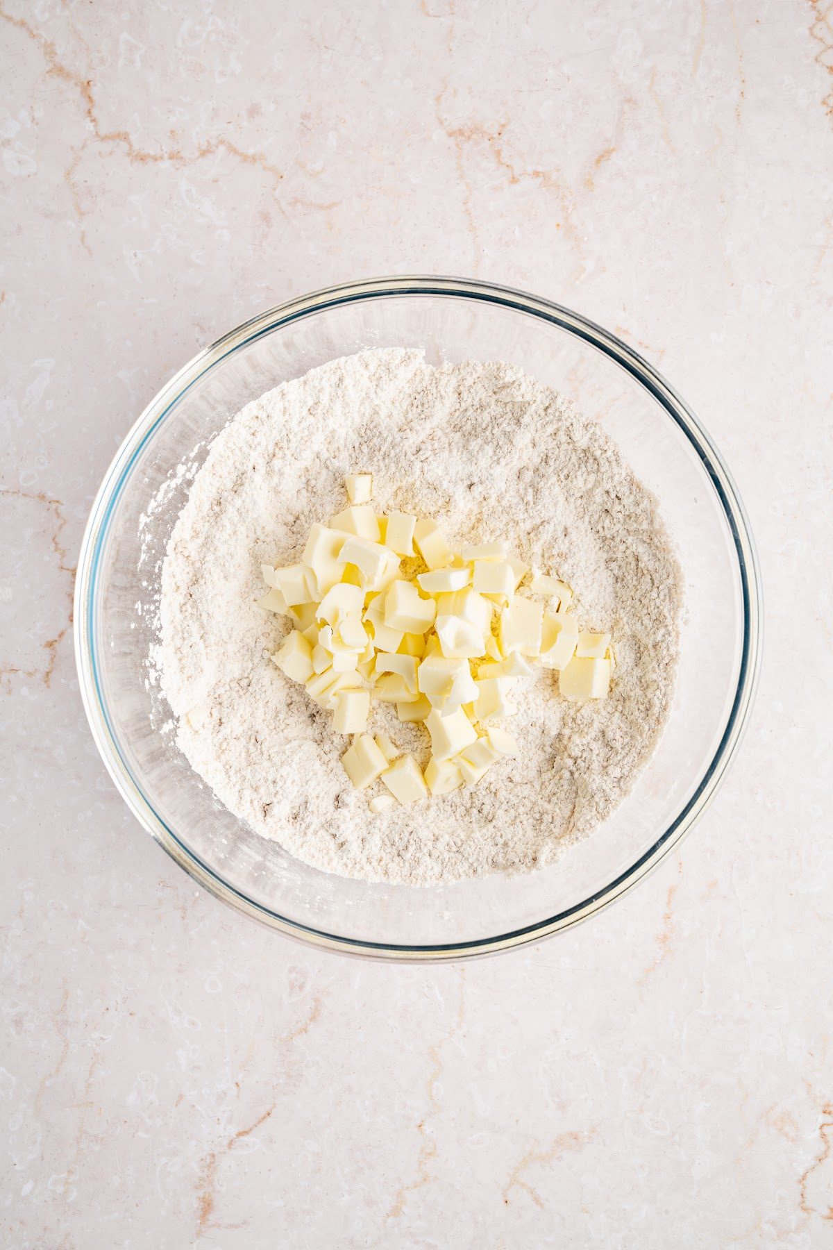 Cubes of cold butter sitting on top of flour, brown sugar, baking powder and salt in a glass bowl
