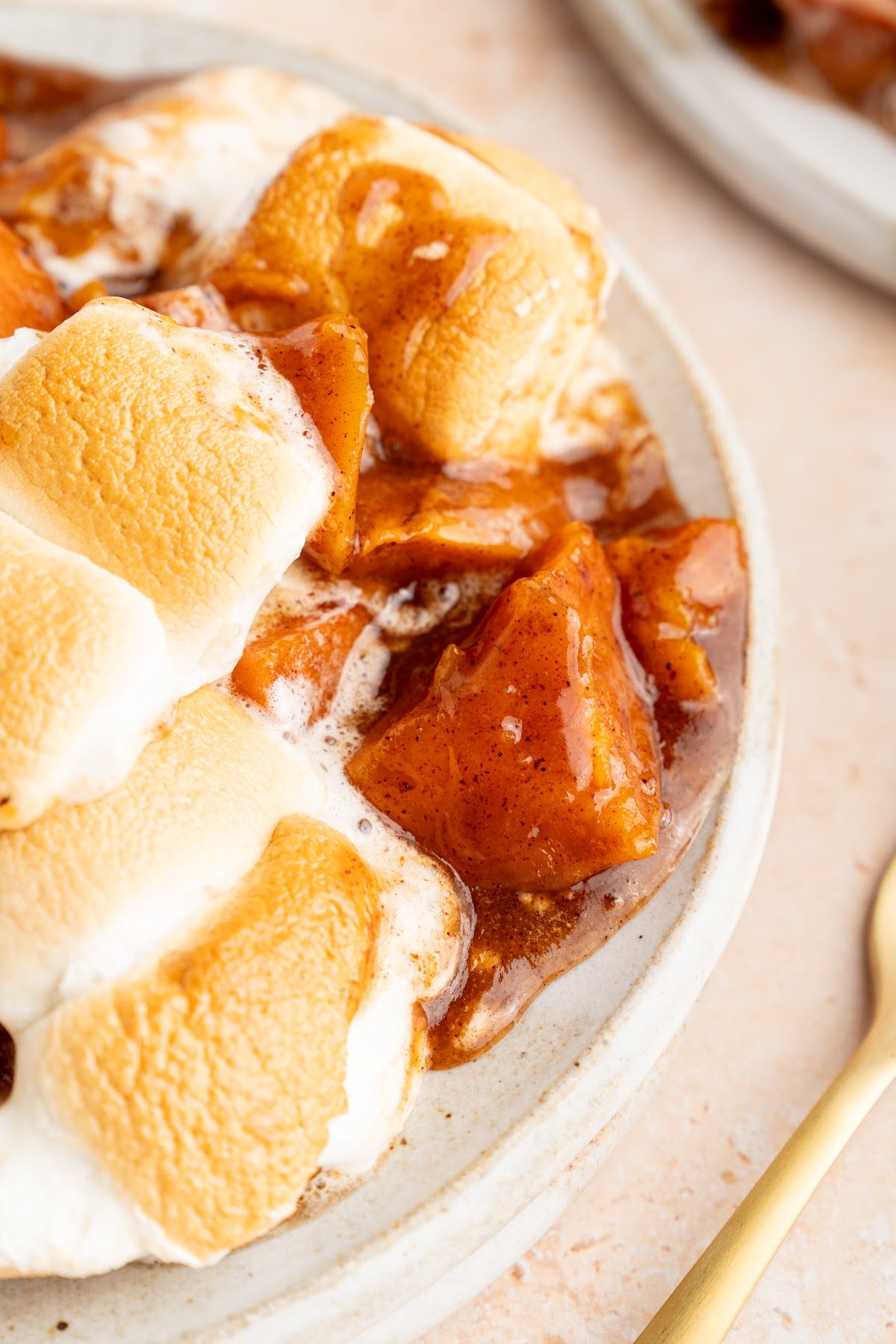 Close-up of glossy candied yam pieces in spiced syrup with toasted marshmallow