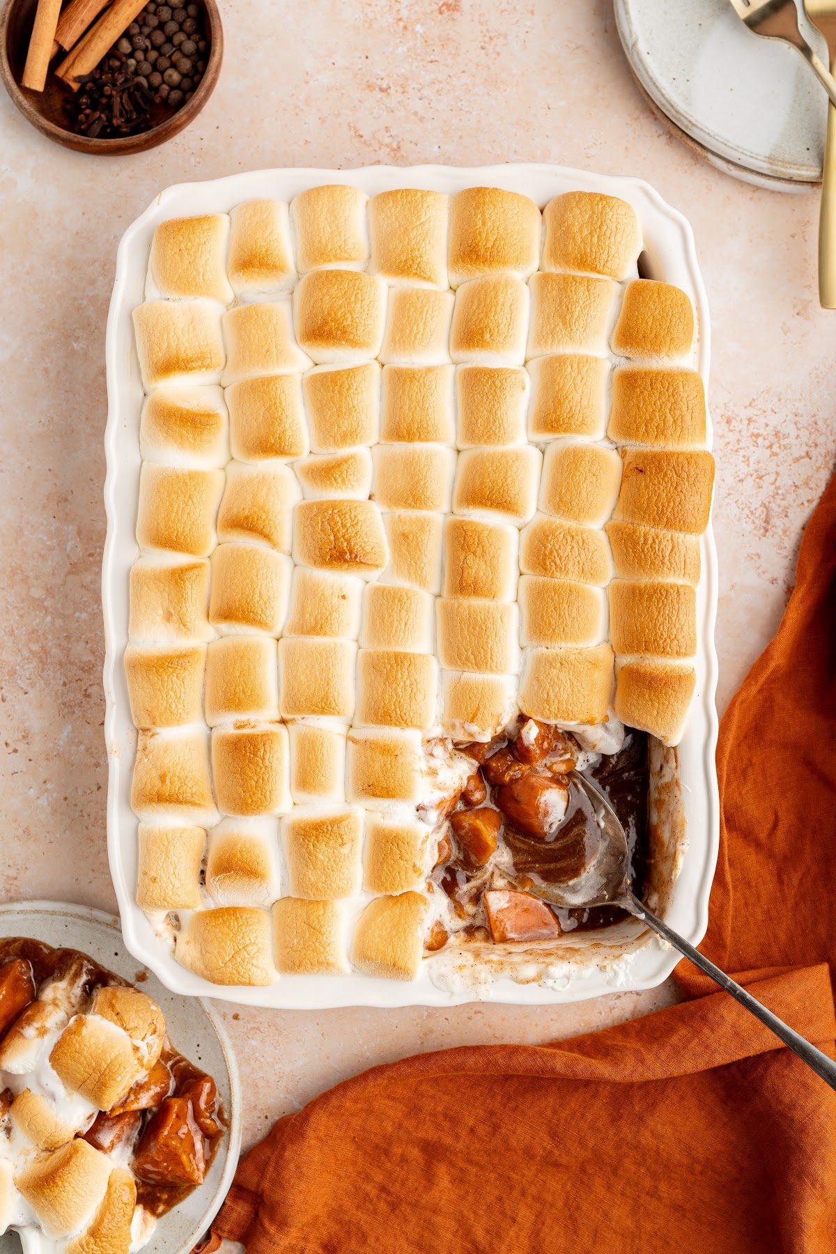 A 13 by 9 pan of candied yams with marshmallows and one scoop taken out showing the yams underneath