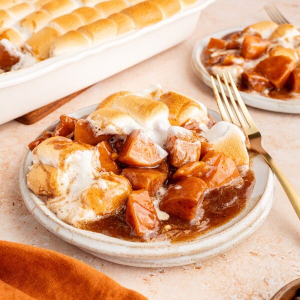 Candied yams with marshmallows served in a small bowl with the baking dish behind