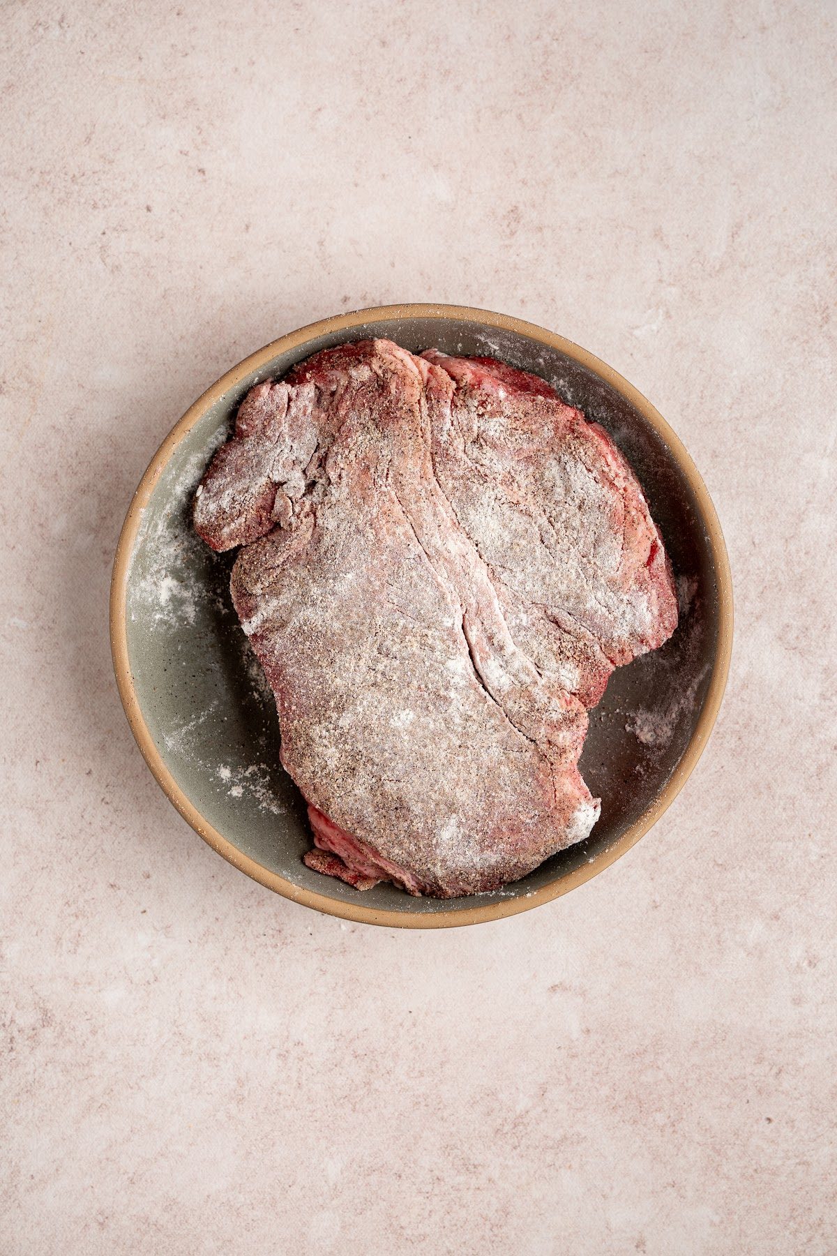 A chuck roast in a bowl seasoned with salt and pepper and dusted with flour before searing