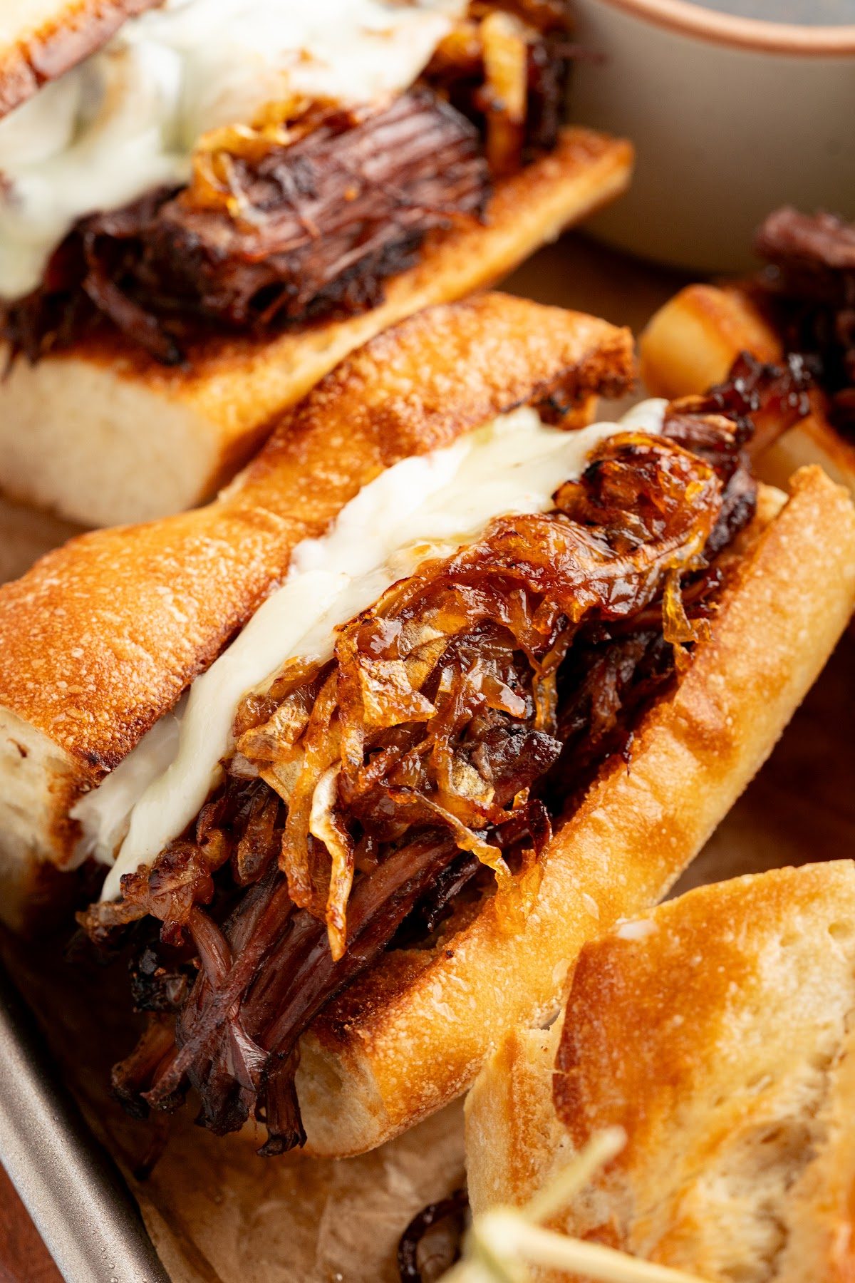 Close-up of a French dip sandwich with shredded beef, caramelized onions and melted provolone on a crusty baguette