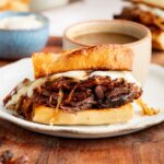 French dip sandwich served on a white plate with a bowl of au jus on the side