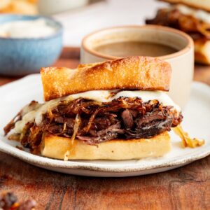 French dip sandwich served on a white plate with a bowl of au jus on the side
