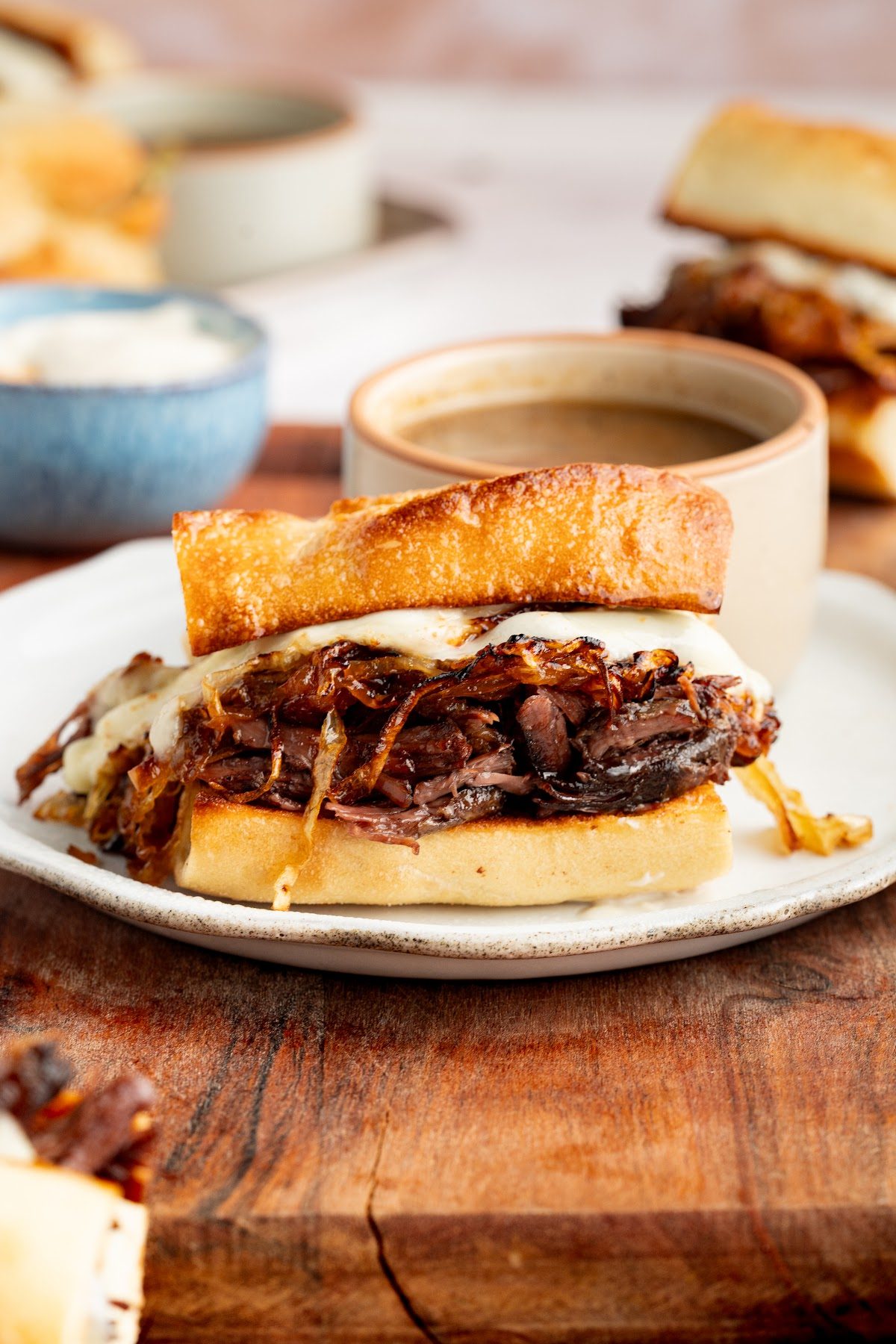 French dip sandwich served on a white plate with a bowl of au jus on the side