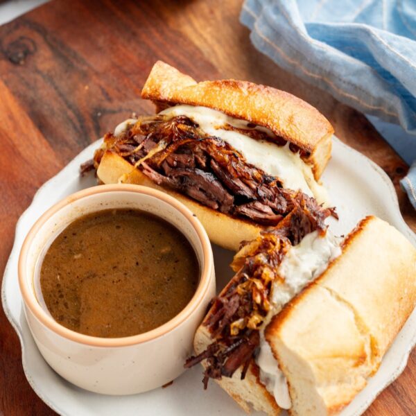A French dip sandwich on a plate with a cup of hot au jus for dipping