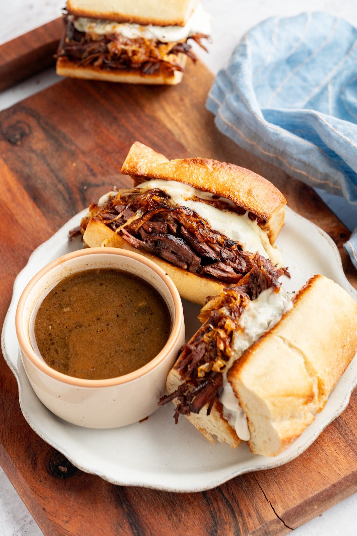 A French dip sandwich on a plate with a cup of hot au jus for dipping