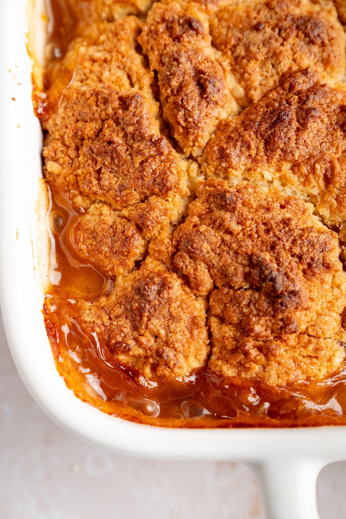 Close-up of a deep golden brown biscuit cobbler top with peach filling bubbling up around the edges