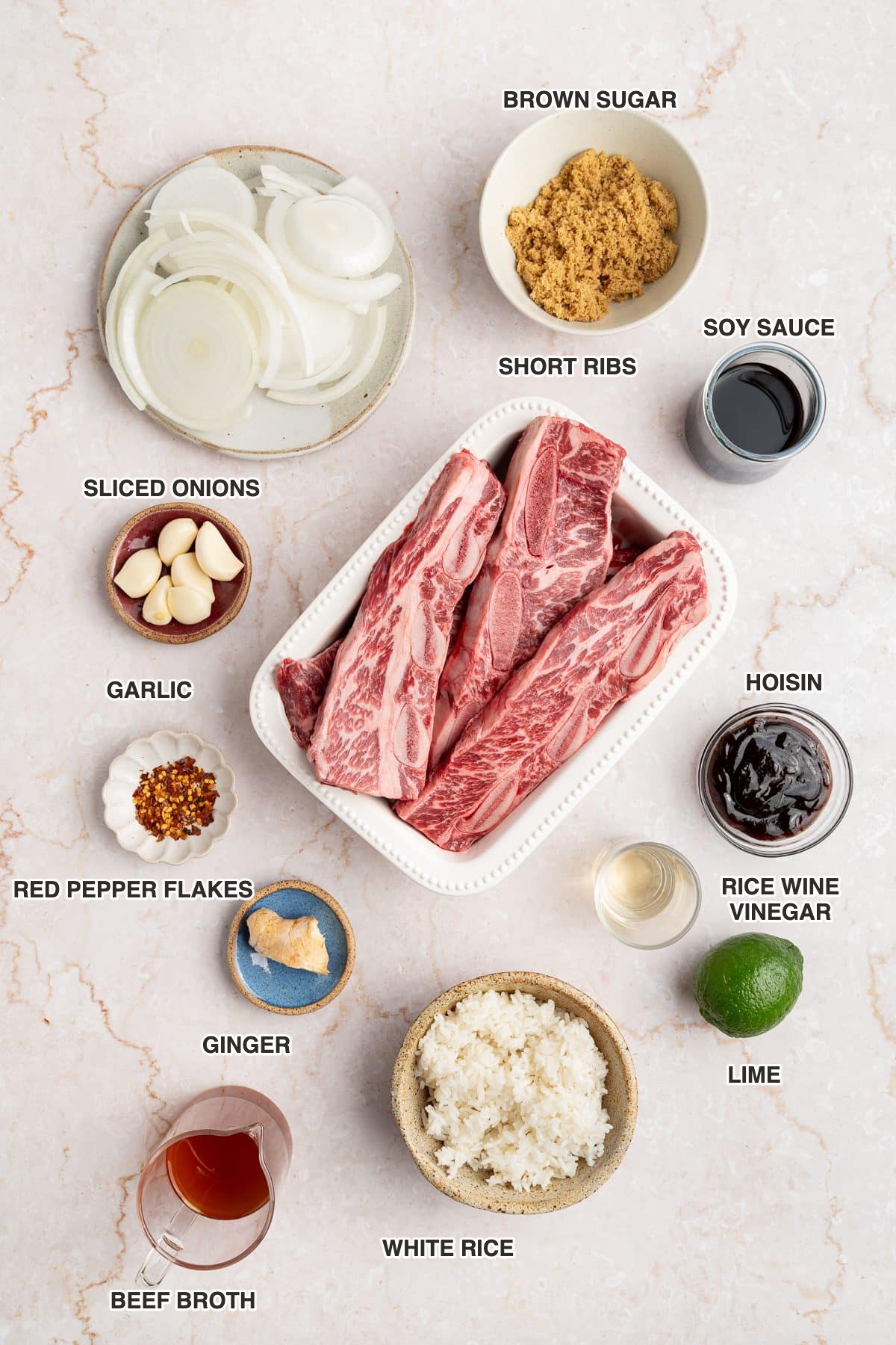 Labeled ingredients for sheet pan Korean short ribs: short ribs, sliced onions, brown sugar, soy sauce, hoisin, rice wine vinegar, garlic, ginger, red pepper flakes, lime, white rice and beef broth