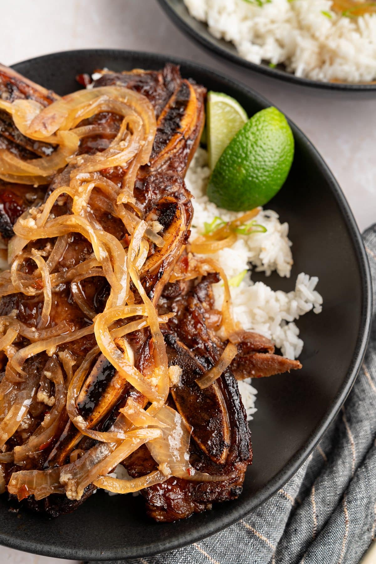 Overhead close-up of jammy onions piled over caramelized short ribs with a lime wedge