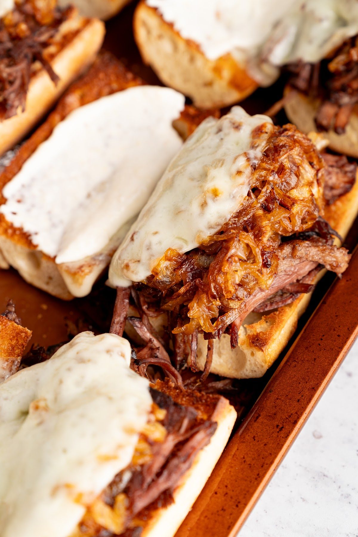 French dip sandwiches on a sheet pan with provolone melted and bubbling over the beef
