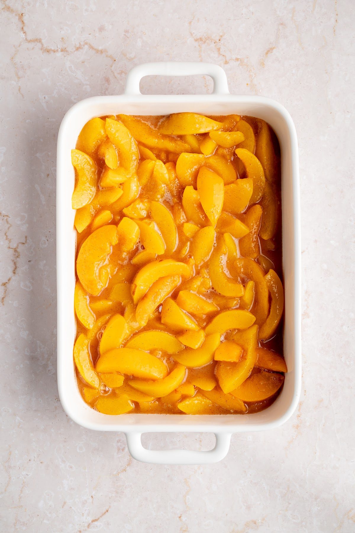 Peach cobbler filling spread in an even layer across a white 9 x 13 inch baking dish
