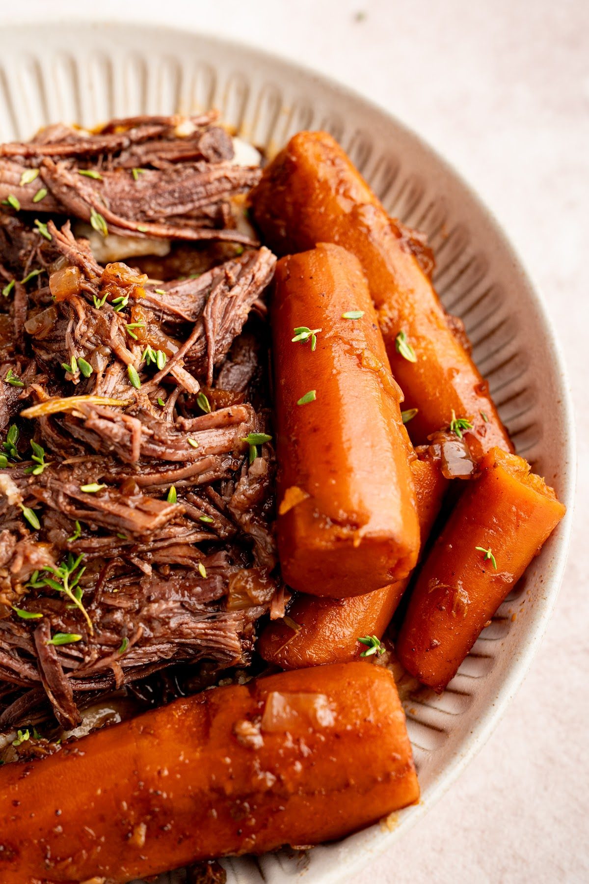 Close-up of shredded pot roast and glossy whole braised carrots in a shallow bowl