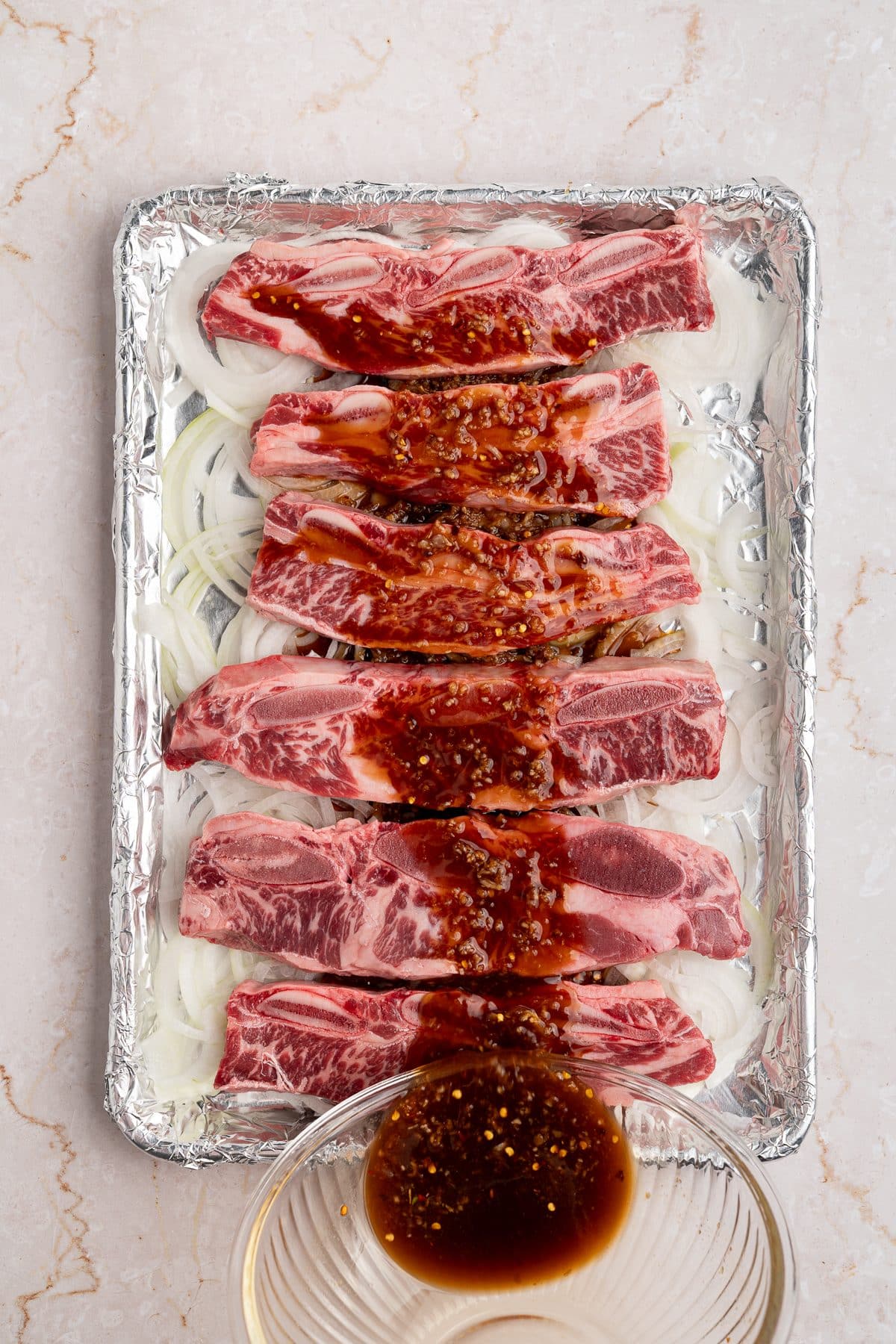 Galbi sauce being poured over raw short ribs on a sheet pan