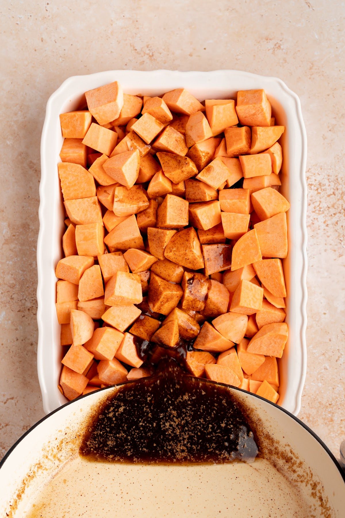 Hot spiced brown butter syrup being poured over cut yams in a baking dish