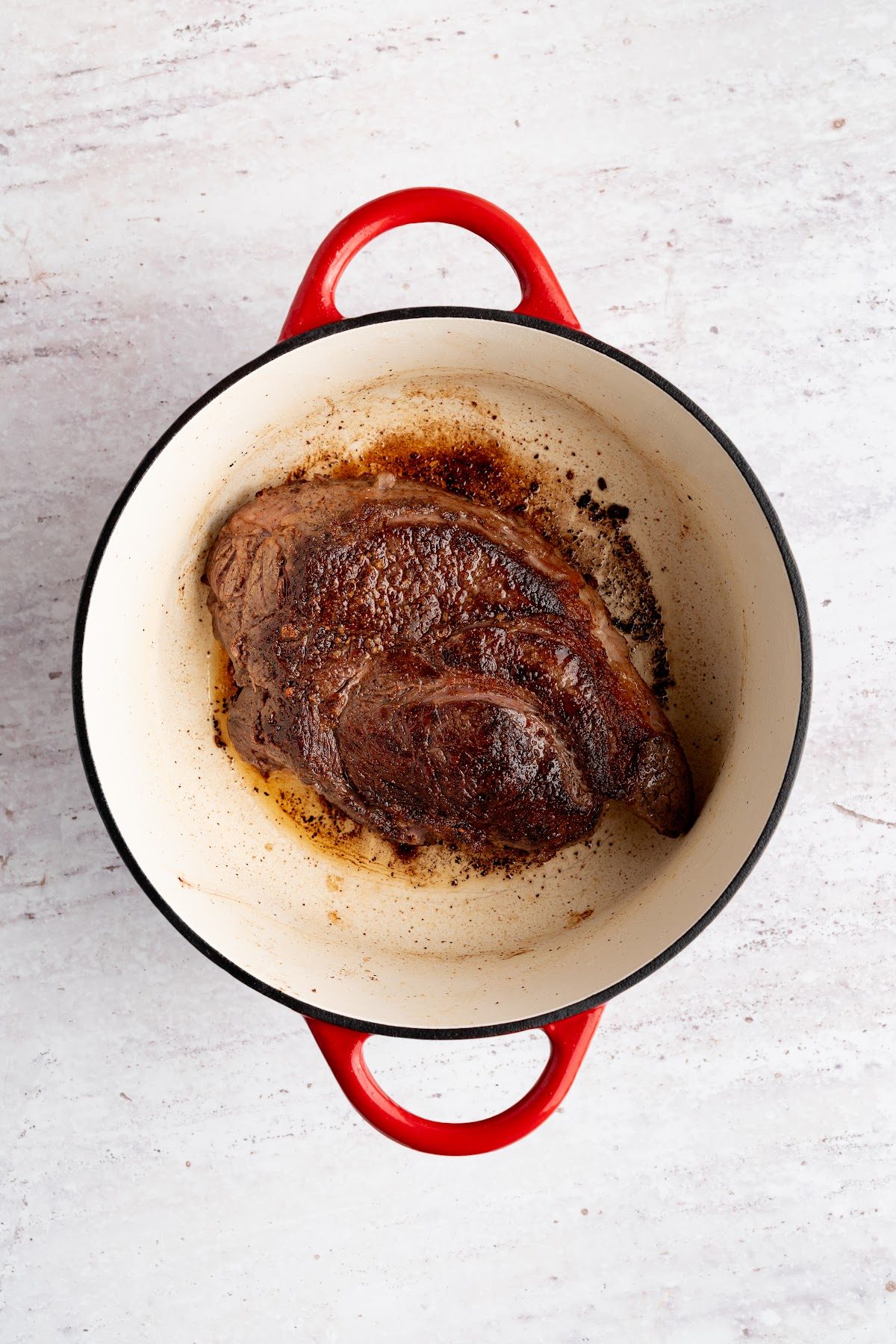 A chuck roast searing deep brown in a red Dutch oven