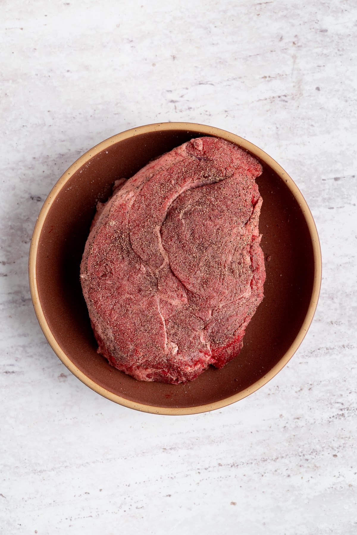 A chuck roast seasoned with salt and pepper in a bowl before searing