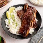 Sheet pan Korean short ribs served over white rice with lime wedges and sliced scallions