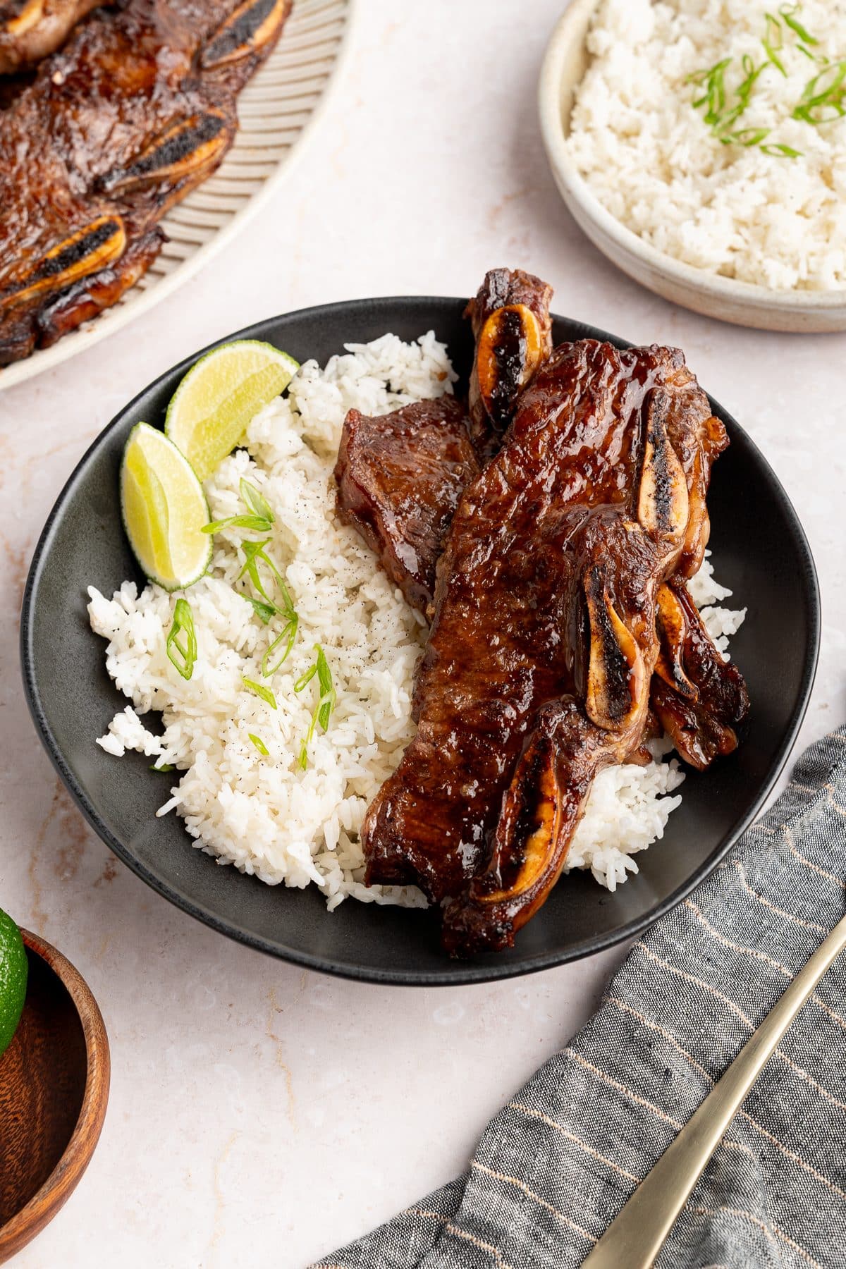 Sheet pan Korean short ribs served over white rice with lime wedges and sliced scallions