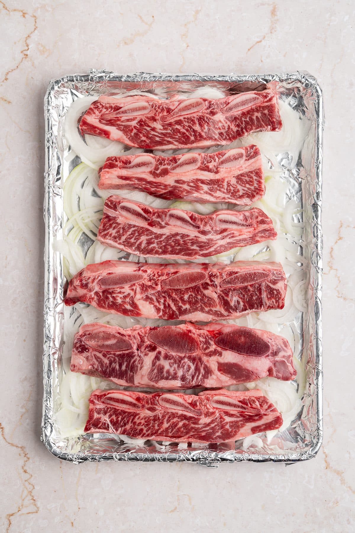 Raw flanken-cut short ribs arranged in a single layer over the sliced onions