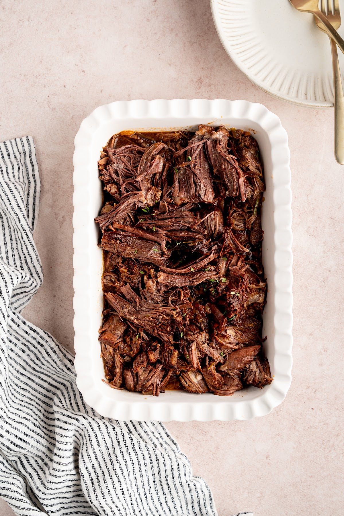 Shredded red wine braised pot roast piled in a white serving dish ready to serve