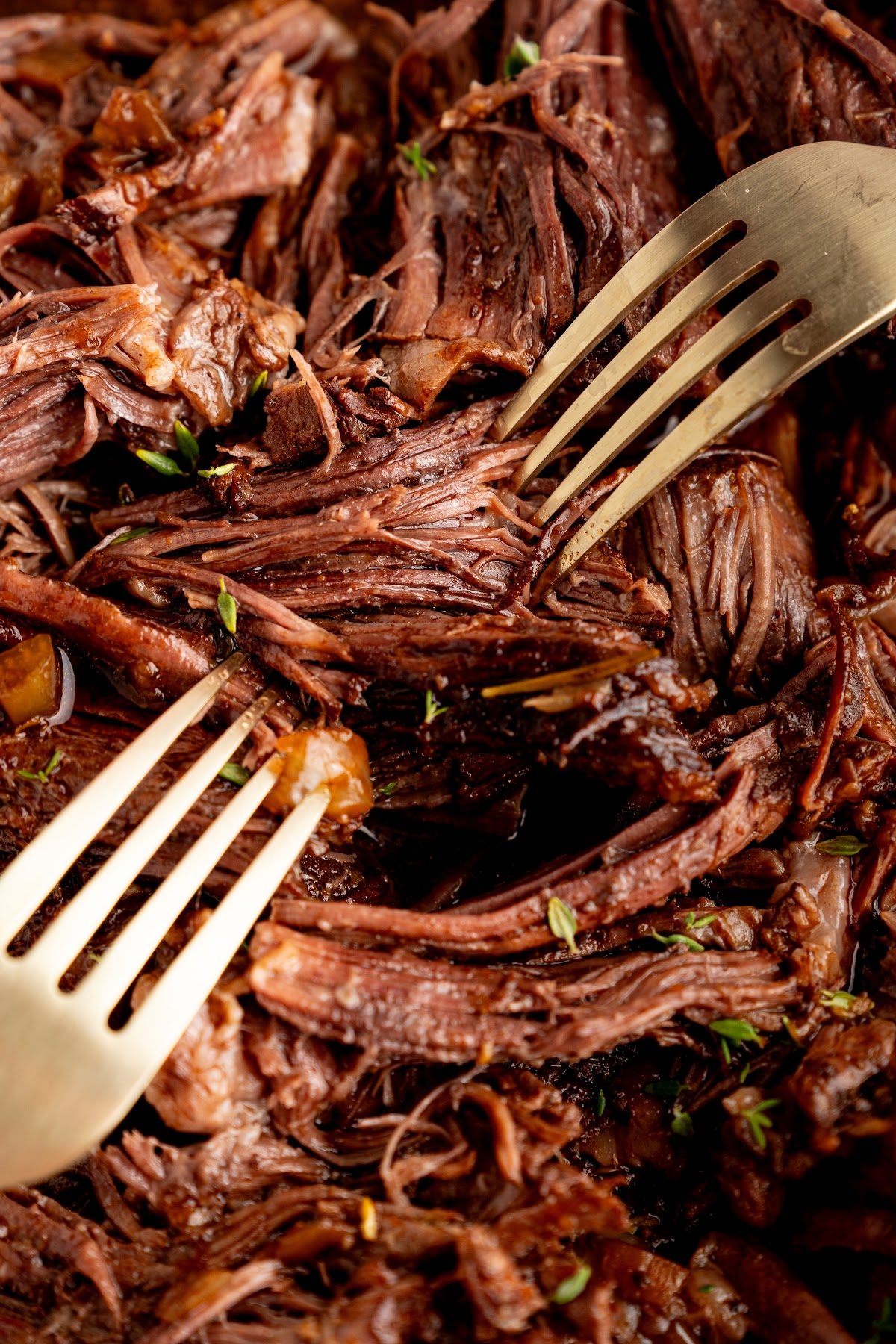 Two forks pulling the braised chuck roast apart into tender shreds