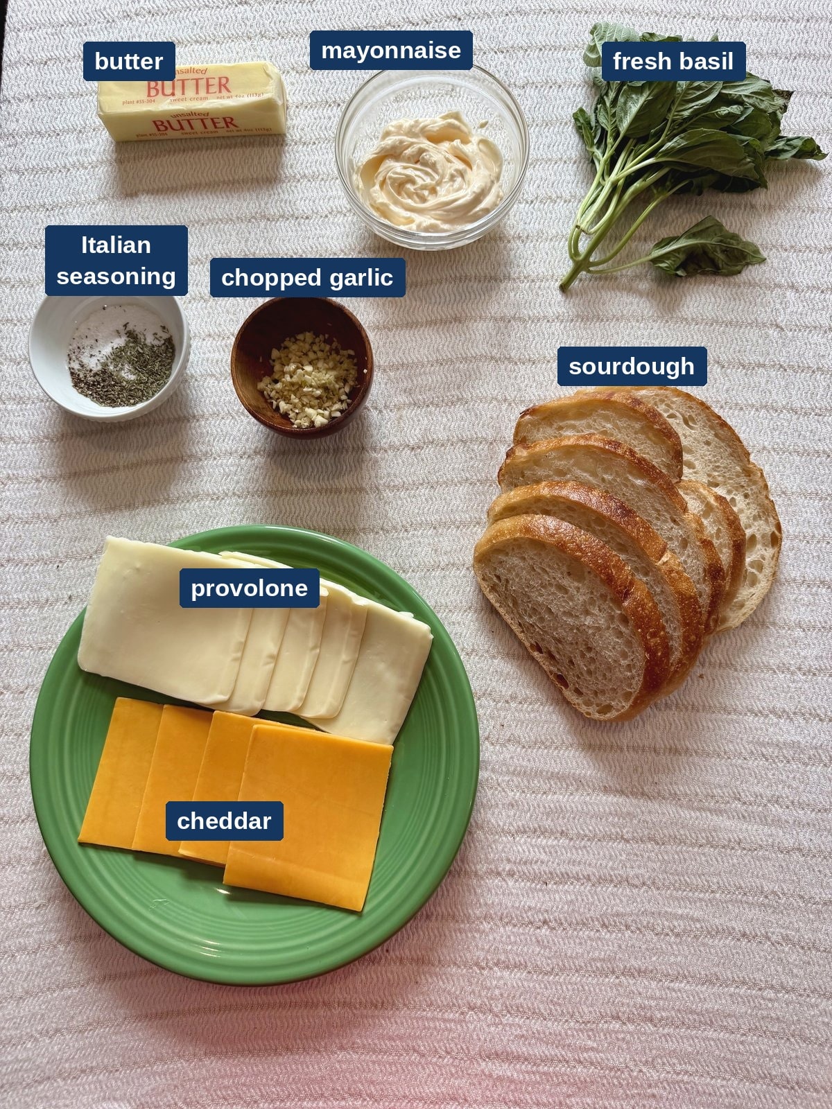 All of the ingredients for a garlic grilled cheese, including sourdough, cheddar, provolone, mayonnaise and fresh basil.